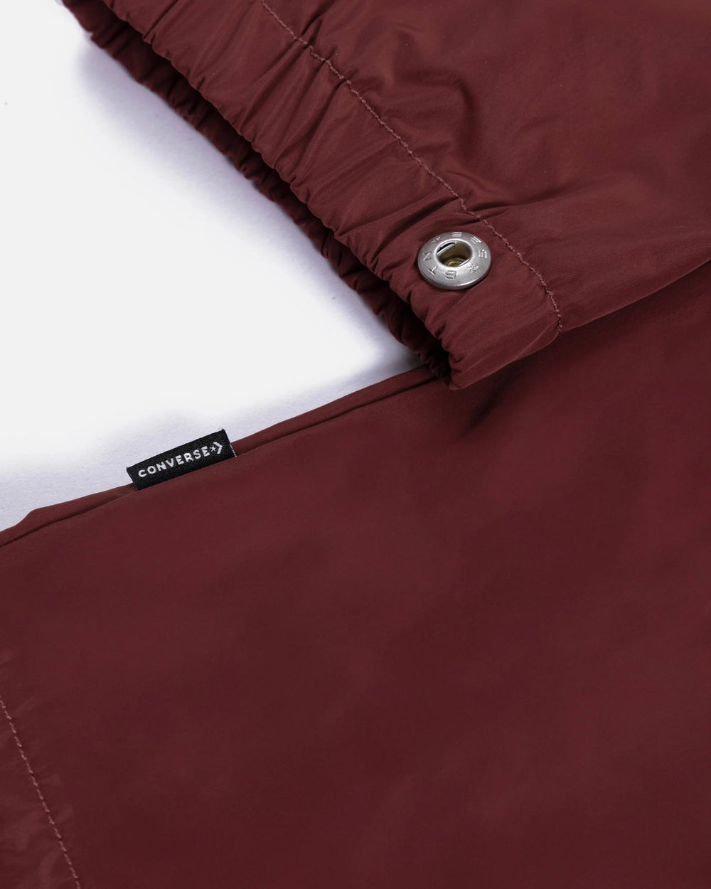 Close-up of the garnet Patta x Converse coaches jacket showing the woven Converse label and grommet detail.