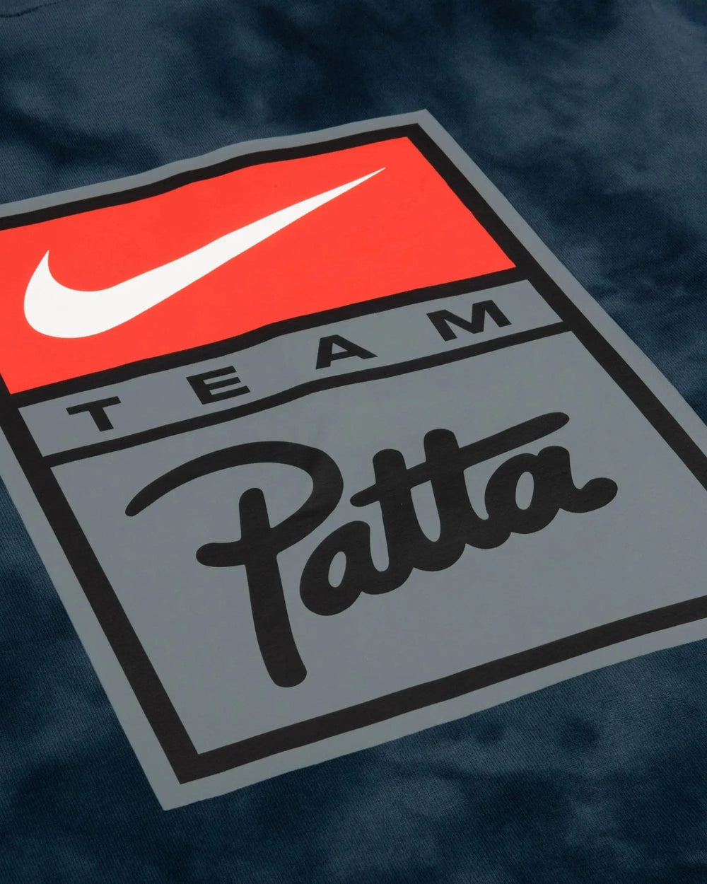 Close-up detail of the Nike Team Patta badge printed on the washed squadron blue NRG t-shirt.